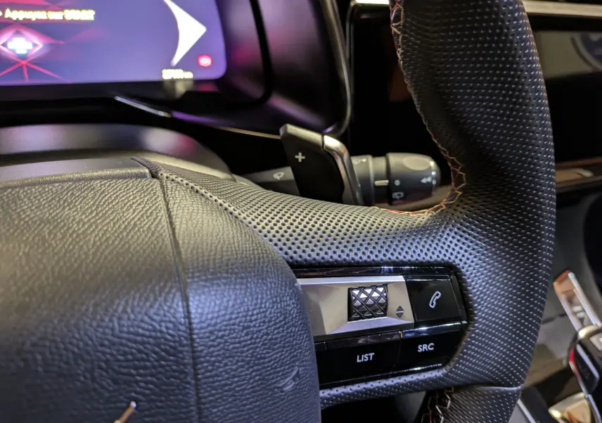 Gros plan sur le volant en cuir perforé noir du DS7 2023 avec commandes intégrées et affichage numérique partiel.