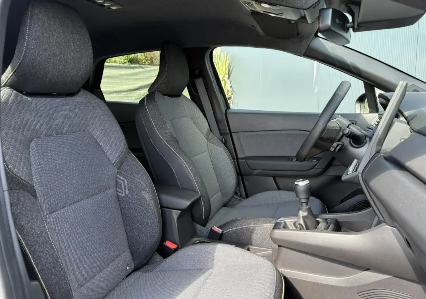 Vue intérieure côté conducteur du Renault Captur 2025, sièges gris et levier de vitesses manuel visible.