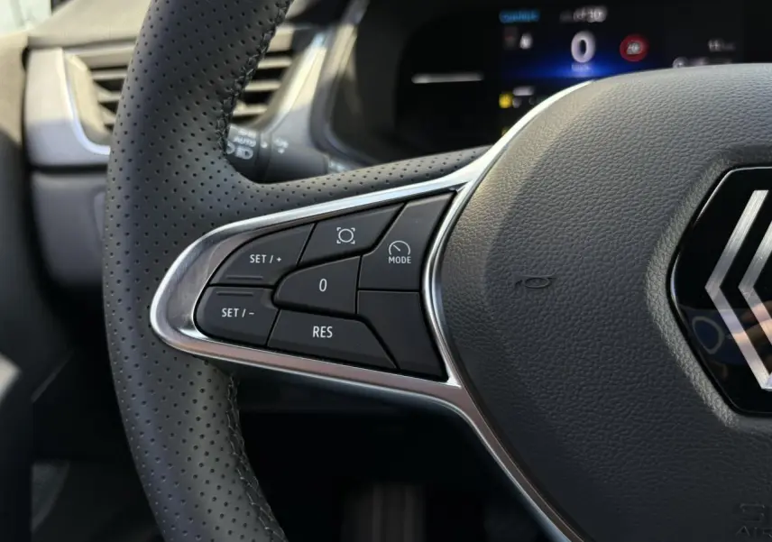 Gros plan sur le volant perforé côté gauche du Renault Captur 2025 avec commandes intégrées et logo central chrome.