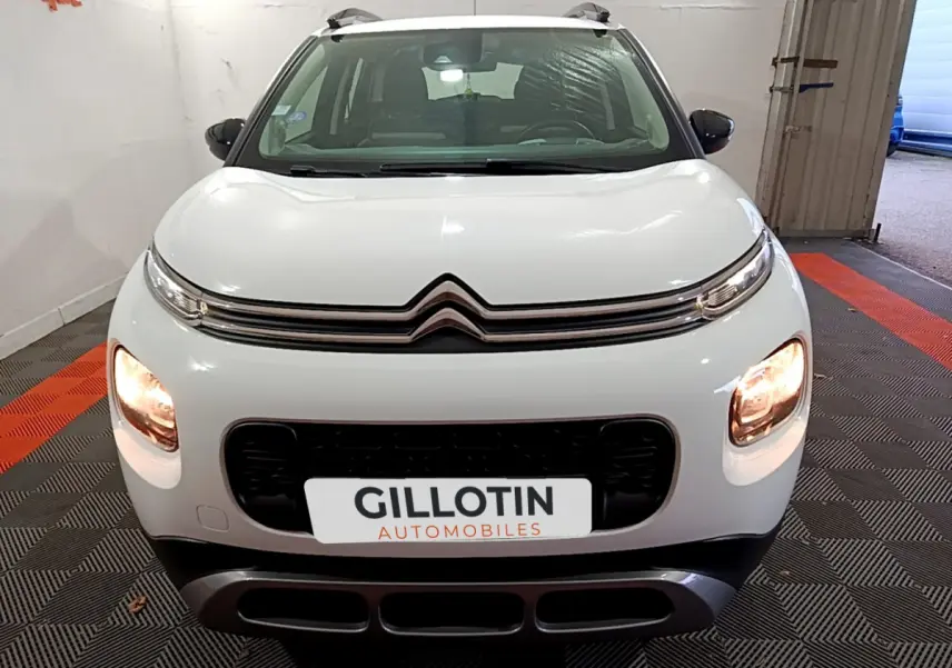 Vue avant d'une Citroën C3 Aircross blanche avec feux allumés et calandre noire dans un garage.