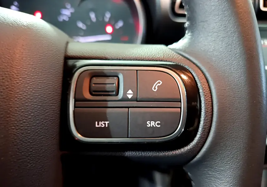 Gros plan sur les commandes gauche du volant cuir noir du Citroën C3 Aircross blanc, avec boutons LIST et SRC visibles.