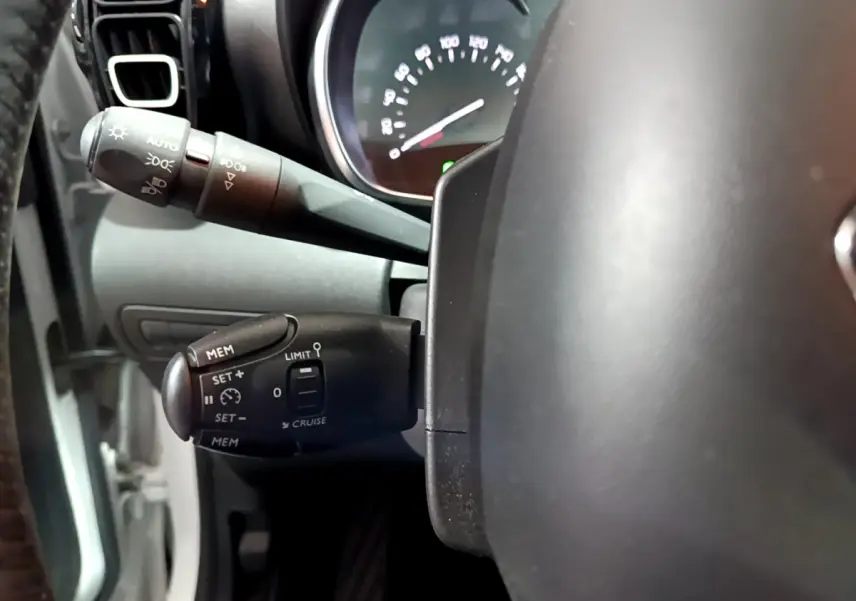Gros plan sur la commande de régulateur de vitesse à gauche du volant dans l’habitacle d’un Citroën C3 Aircross blanc 2019.