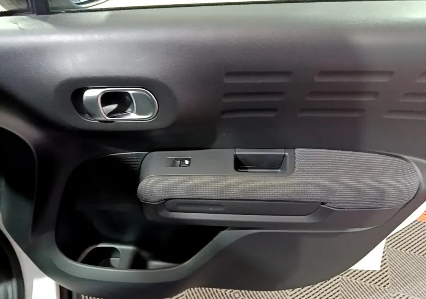 Vue rapprochée de la porte intérieure côté droit du Citroën C3 Aircross blanc, avec poignée argentée et accoudoir tissu.