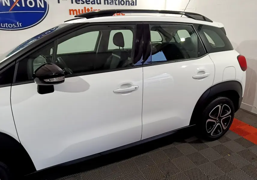 Vue latérale droite d'un Citroën C3 Aircross blanc avec rétroviseurs noirs et barres de toit noires.