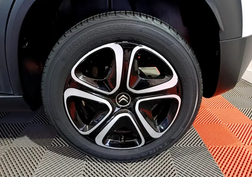 Gros plan sur la roue avant droite du Citroën C3 Aircross blanc, jante alliage noire et argentée au design moderne.