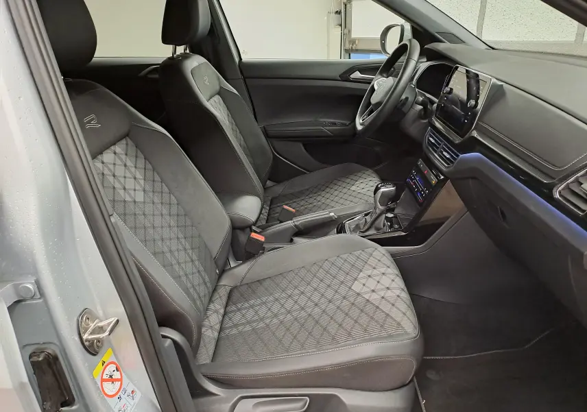Vue intérieure côté conducteur du Volkswagen T-Cross 2025 R-Line Edition, sièges noirs avec surpiqûres et volant multifonction.