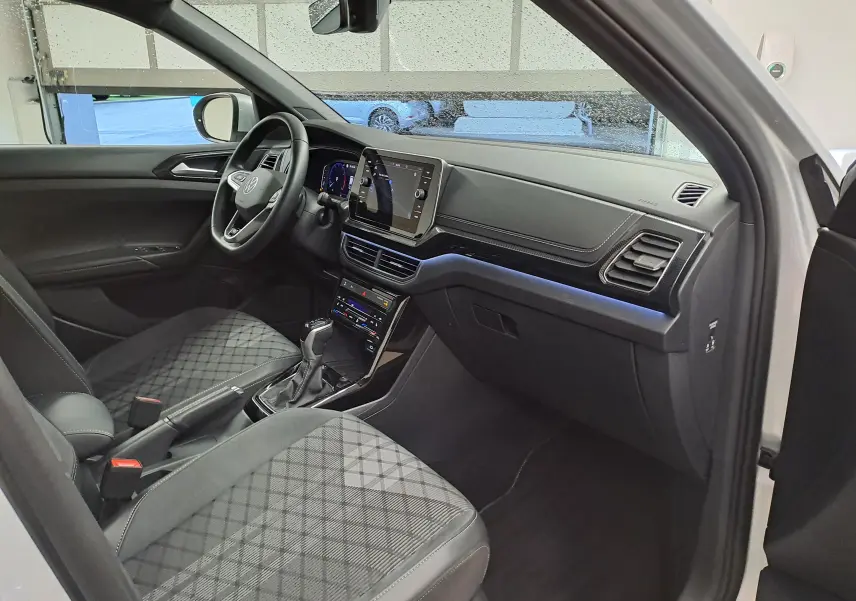 Vue intérieure côté conducteur du Volkswagen T-Cross 2025 argent, avec tableau de bord moderne et sièges tissu à motif géométrique.