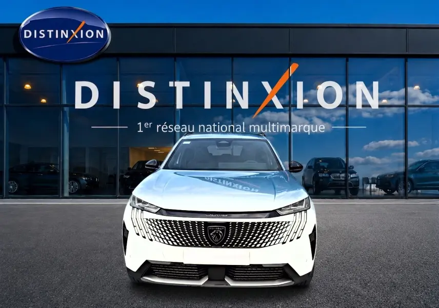 Vue frontale d'un Peugeot 5008 blanc garé devant une vitrine avec logo Distinxion en arrière-plan.