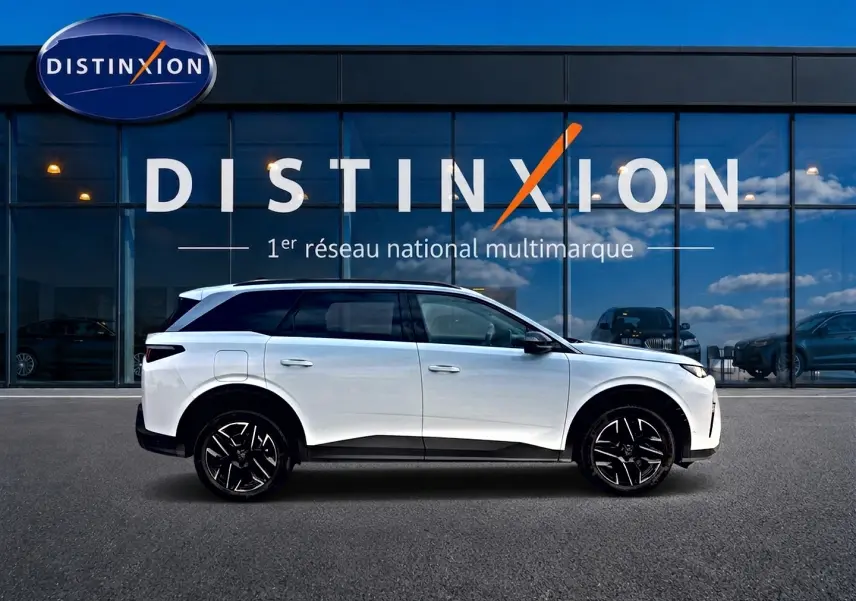 Vue de profil côté gauche d’un Peugeot 5008 blanc avec jantes alliage noires devant une vitrine Distinxion.