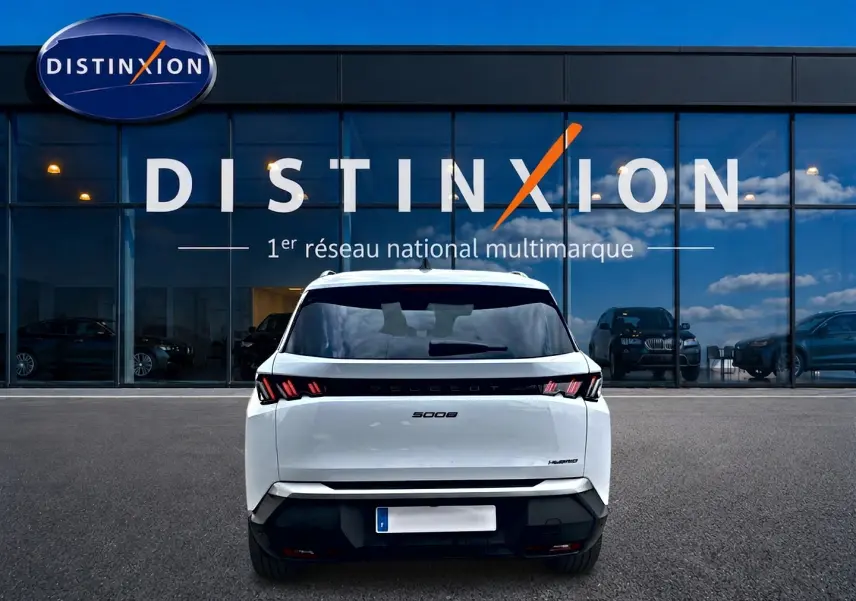 Vue arrière d'un Peugeot 5008 blanc hybride 2025 avec feux LED distinctifs, stationné devant une vitrine Distinxion.