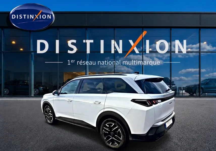 Peugeot 5008 Hybrid blanc en 3/4 arrière droit, avec jantes alu noires et toit noir devant une vitrine Distinxion.