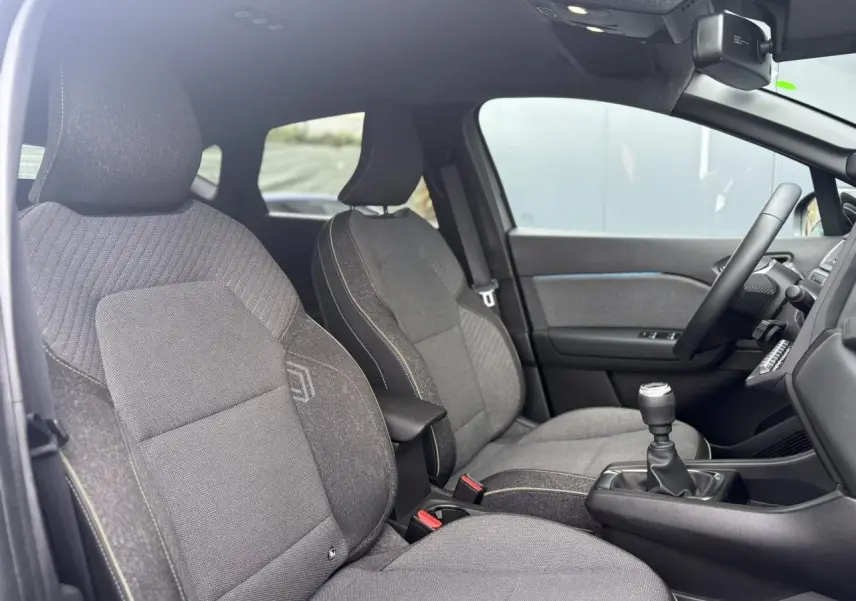 Vue intérieure côté conducteur du Renault Captur TCE 100 Techno 2025, sièges gris et levier de vitesse manuel visible.