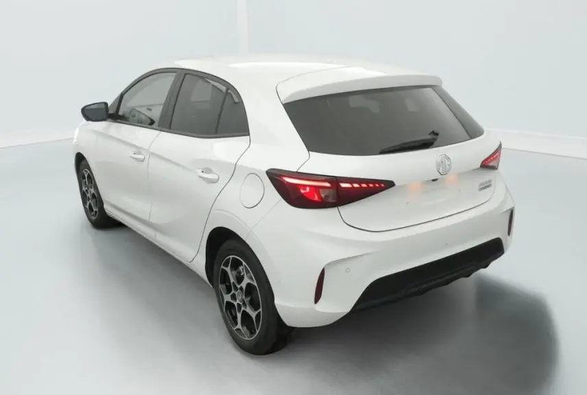 Vue 3/4 arrière gauche de la MG3 1.5 L HYBRID+ 195 CH Luxury en blanc Dover avec feux arrière allumés et jantes noires.