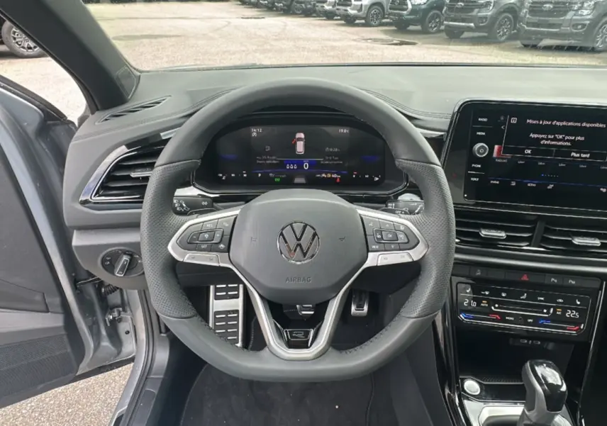 Vue intérieure centrée sur le volant du Volkswagen T-Roc gris pyrite 2025, avec tableau de bord numérique et écran tactile.