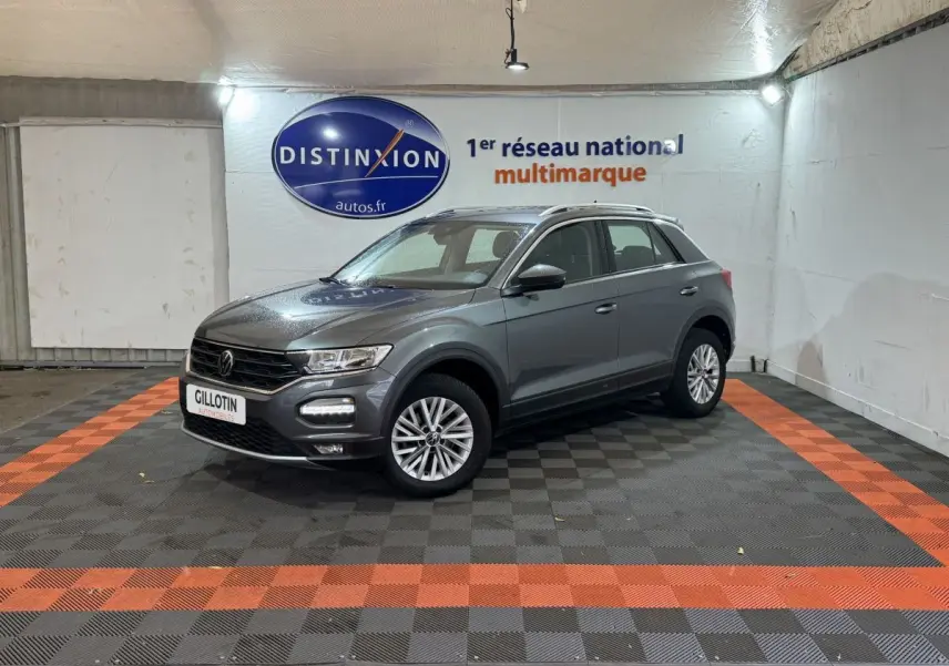 Volkswagen T-Roc gris foncé vue 3/4 avant droit dans un showroom avec sol noir et orange.