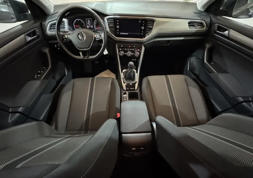 Vue intérieure avant du Volkswagen T-Roc 1.6 TDI 115 Lounge Business, montrant tableau de bord, volant cuir et sièges tissu gris.