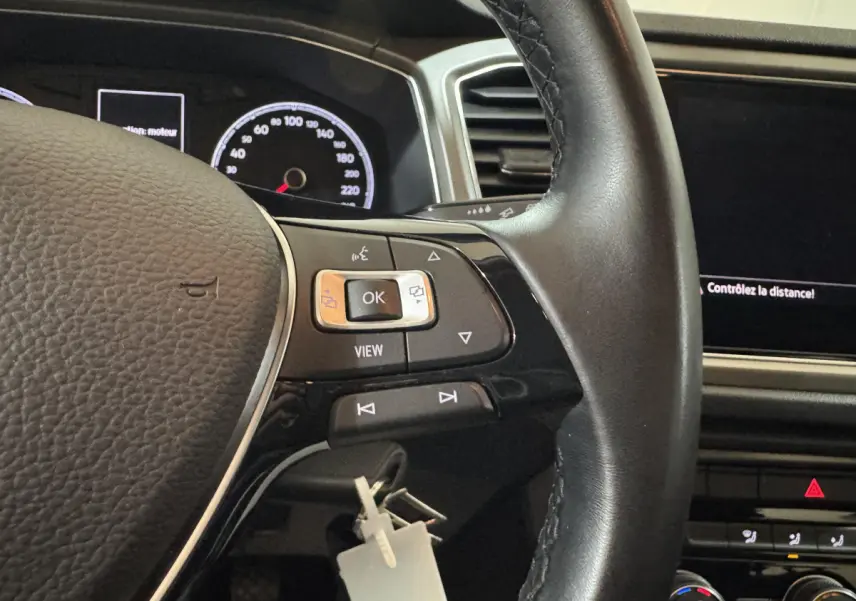 Gros plan sur le volant cuir noir et le tableau de bord numérique du Volkswagen T-Roc 1.6 TDI 2021, intérieur gris foncé.