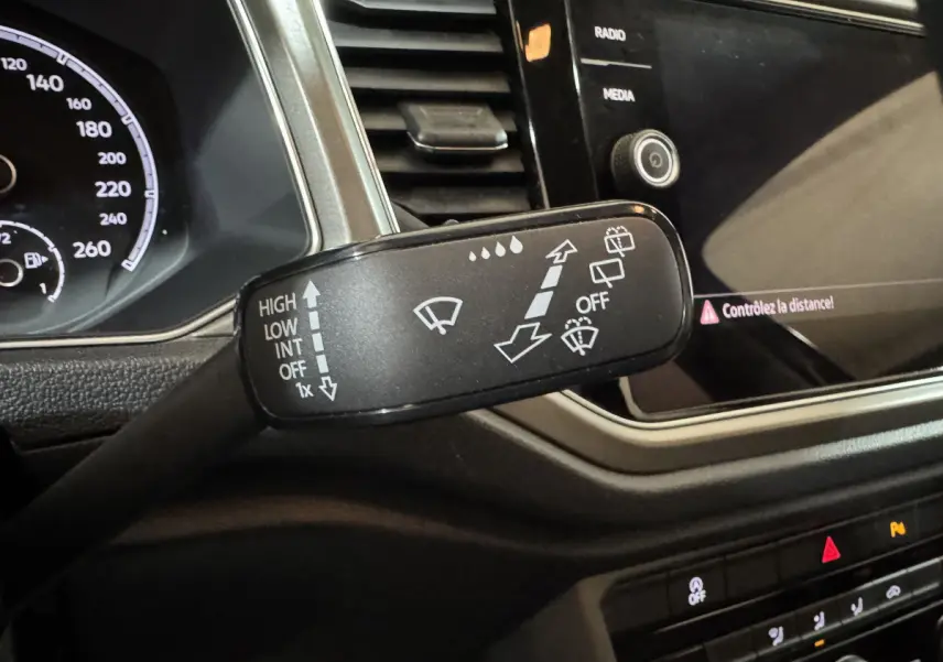 Gros plan sur la commande des essuie-glaces dans l’habitacle du Volkswagen T-Roc gris foncé, tableau de bord et écran tactile visibles.