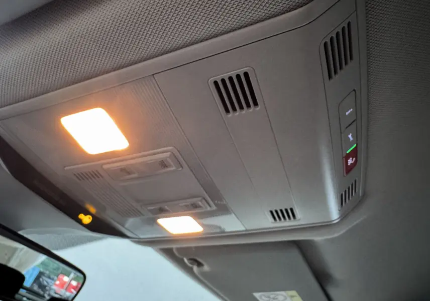 Plafonnier intérieur allumé vu de dessous dans un Volkswagen T-Roc gris foncé, avec commandes et aérations visibles.