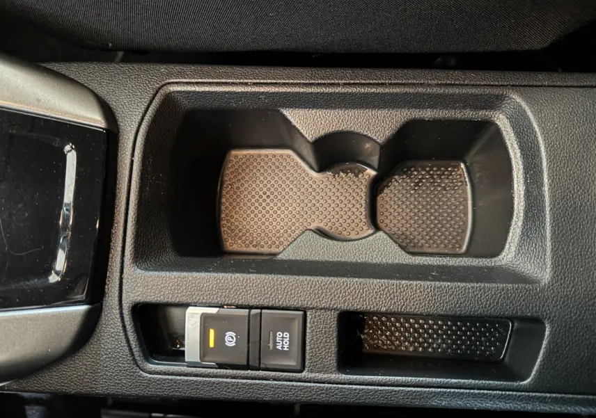 Gros plan sur la console centrale noire du Volkswagen T-Roc 1.6 TDI, avec porte-gobelets et frein à main électrique activé.