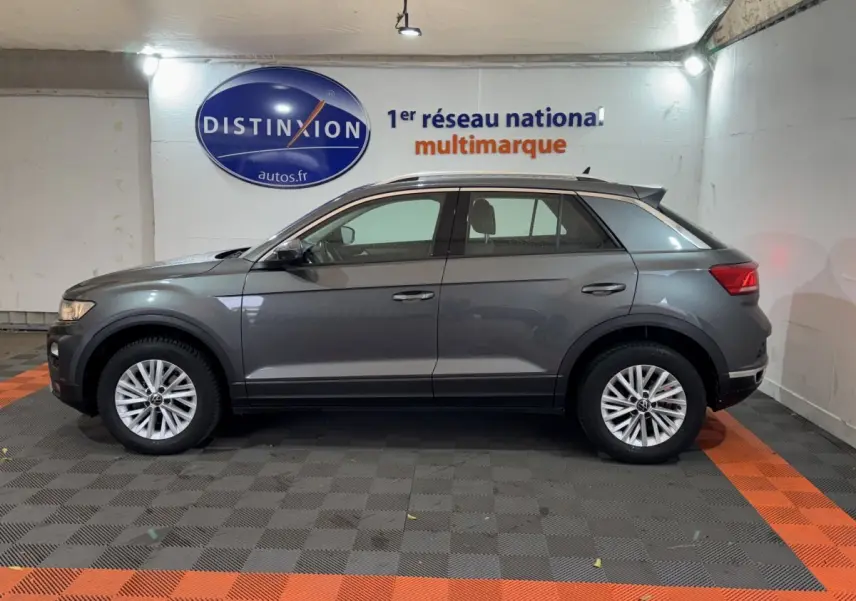 Profil côté gauche d'un Volkswagen T-Roc gris foncé 2021 stationné en intérieur avec jantes alliage visibles.