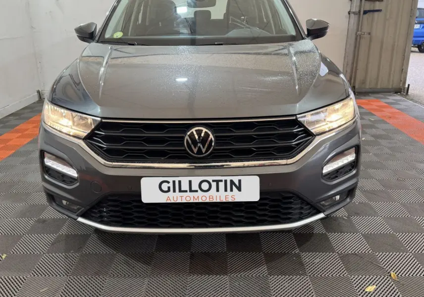 Vue avant rapprochée du Volkswagen T-Roc gris foncé 2021 avec calandre noire et phares allumés.