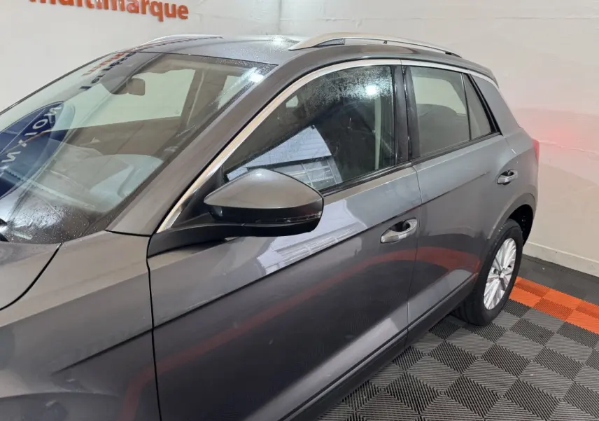 Vue côté gauche du Volkswagen T-Roc gris foncé, mettant en valeur la porte avant et le rétroviseur avec clignotant intégré.