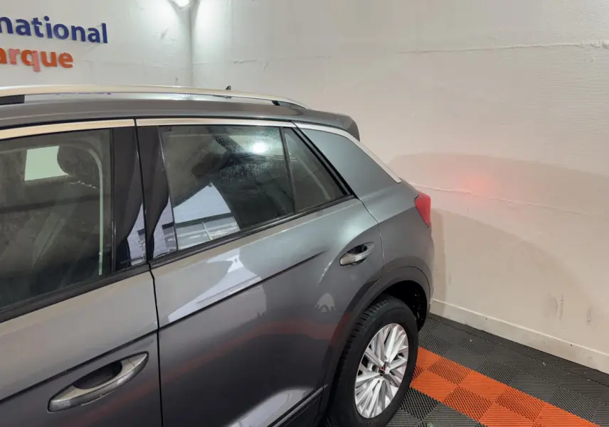 Vue côté arrière droit d’un Volkswagen T-Roc gris foncé, mettant en valeur la porte arrière et la roue arrière.
