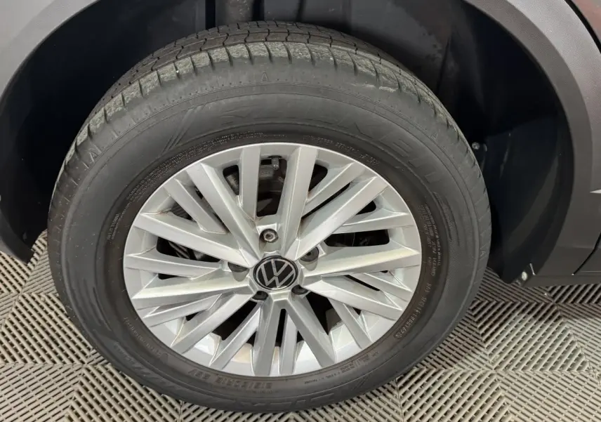 Gros plan sur la roue avant droite d’un Volkswagen T-Roc gris foncé, mettant en valeur la jante alliage et le logo VW.
