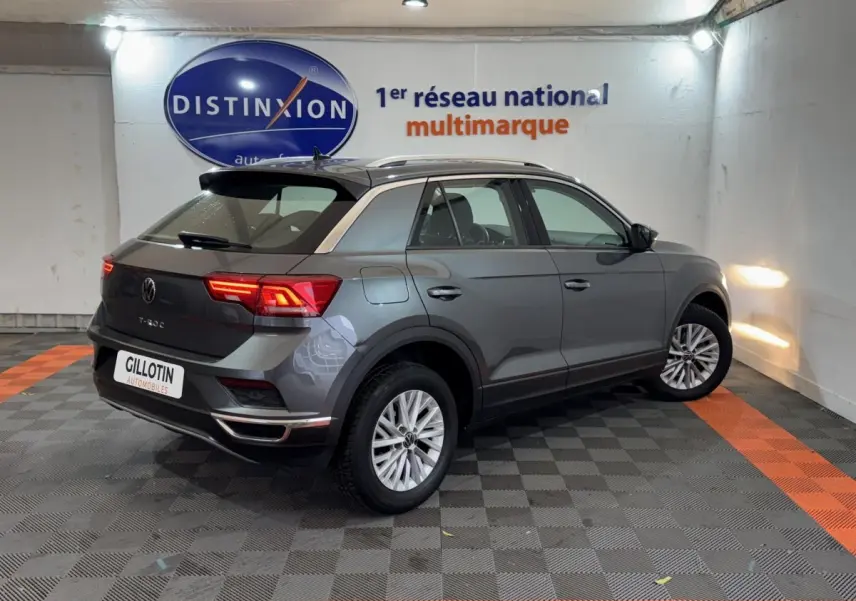 Volkswagen T-Roc gris foncé vue 3/4 arrière droit en intérieur avec feux arrière allumés.