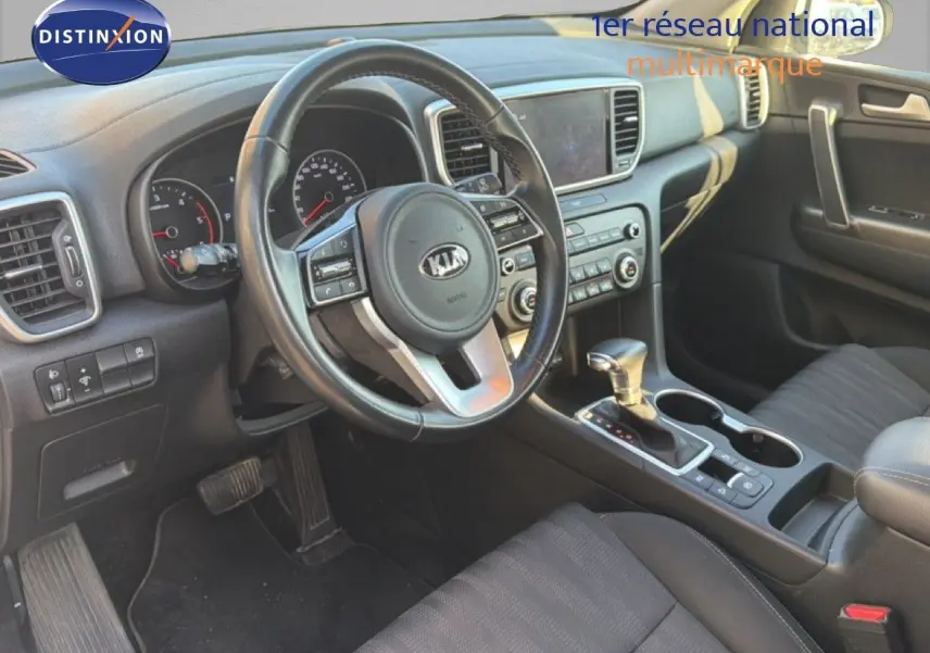 Vue intérieure côté conducteur du Kia Sportage 2021, tableau de bord noir avec volant multifonction et console centrale.