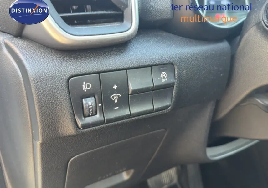 Gros plan sur les commandes de réglage des phares et désactivation du système start-stop dans un Kia Sportage blanc nacré 2021.