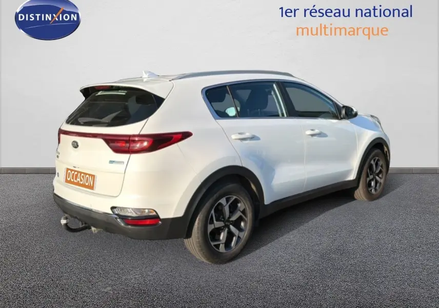 Vue 3/4 arrière droite du Kia Sportage blanc nacré avec jantes alliage bicolores et attelage visible.