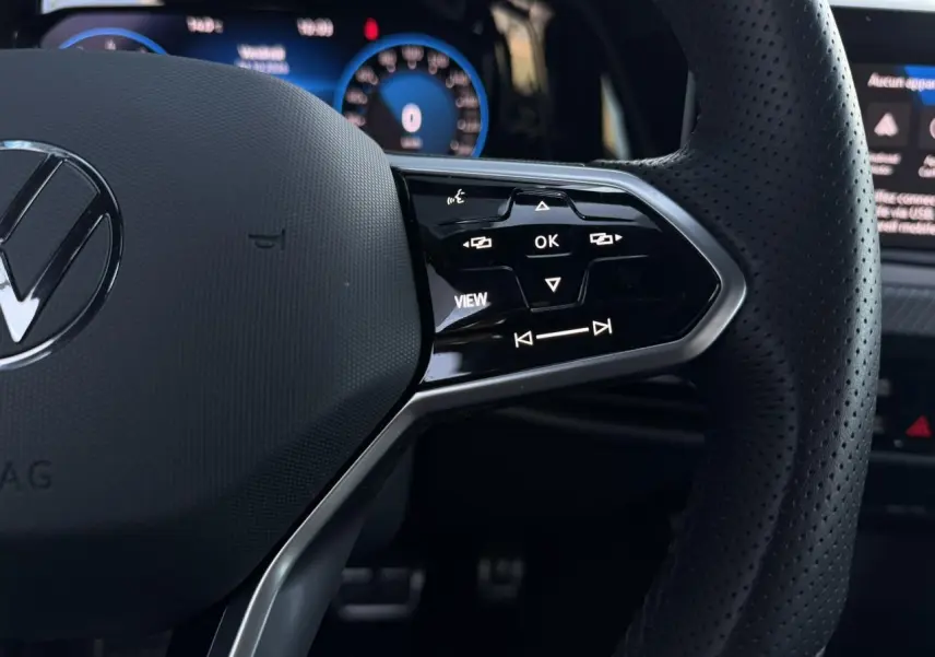 Gros plan sur le volant cuir perforé de la Volkswagen Golf 8 R-Line 2024 avec commandes multifonctions et affichage digital bleu.