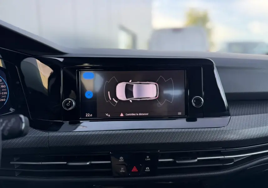 Vue rapprochée de l'écran tactile central noir affichant l'aide au stationnement d'une Volkswagen Golf 8 gris Urano.