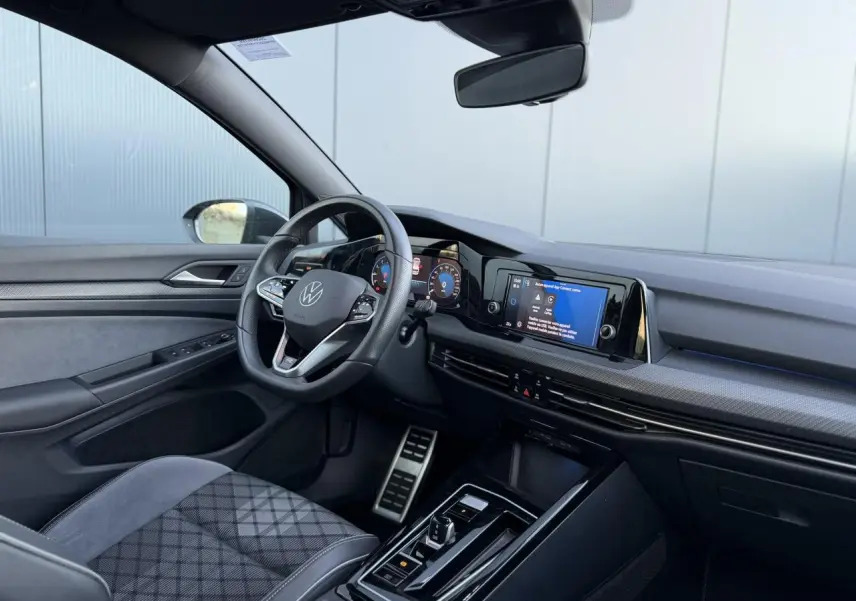 Vue intérieure côté conducteur de la Volkswagen Golf 8 R-Line 2024, avec sellerie tissu gris et tableau de bord numérique.