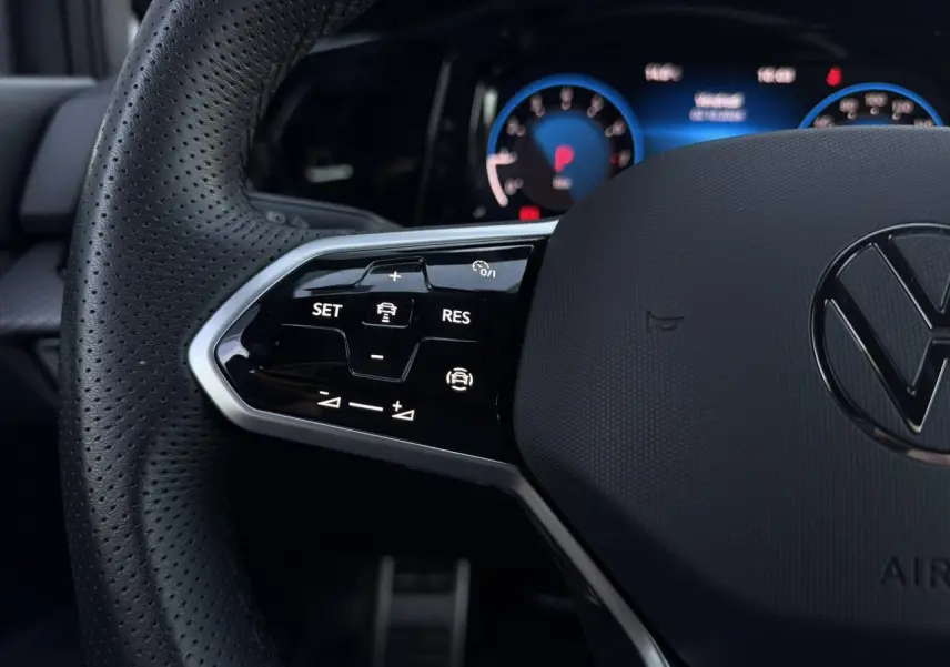 Gros plan sur le volant cuir noir perforé de la Volkswagen Golf 8 R-Line avec commandes multifonctions et tableau de bord digital bleu.