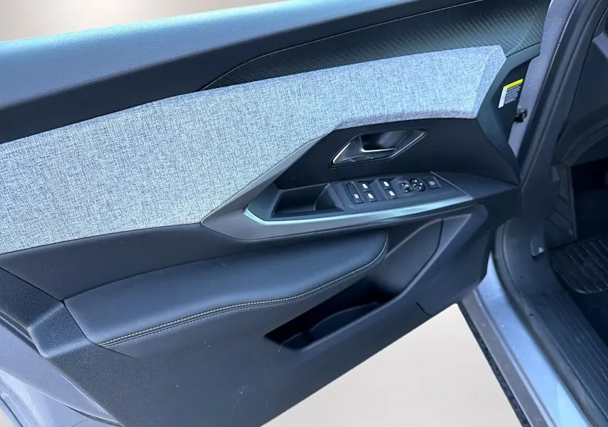 Vue rapprochée de la porte avant gauche du Peugeot 5008 gris artense, montrant les commandes des vitres et le revêtement tissu.