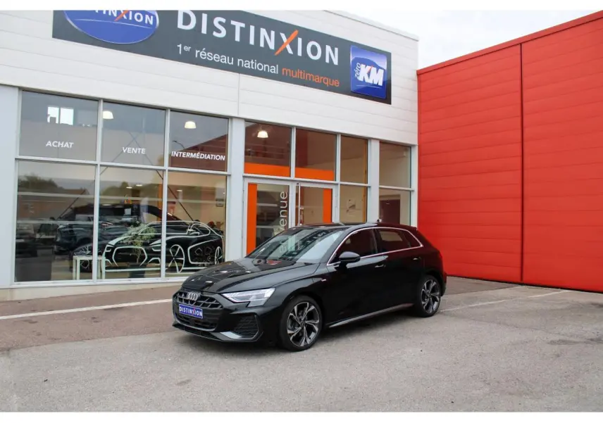 Audi A3 Sportback noir mito metal vue 3/4 avant avec jantes 5 branches et calandre S line devant un bâtiment rouge.