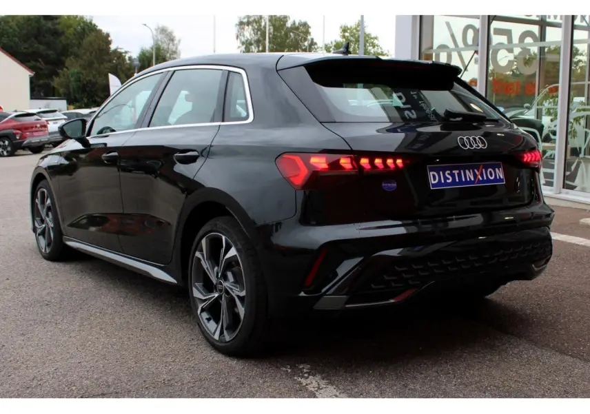 Audi A3 Sportback noir mito metal vue 3/4 arrière droit avec feux arrière LED allumés et jantes 18 pouces graphiques.