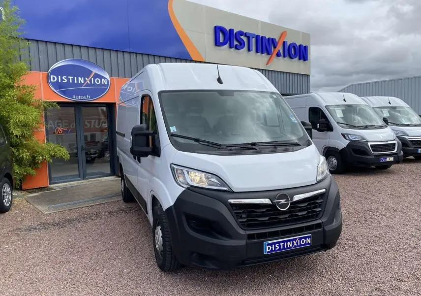 Vue 3/4 avant d'un Opel Movano Fourgon blanc stationné devant un garage avec logo Distinxion visible.