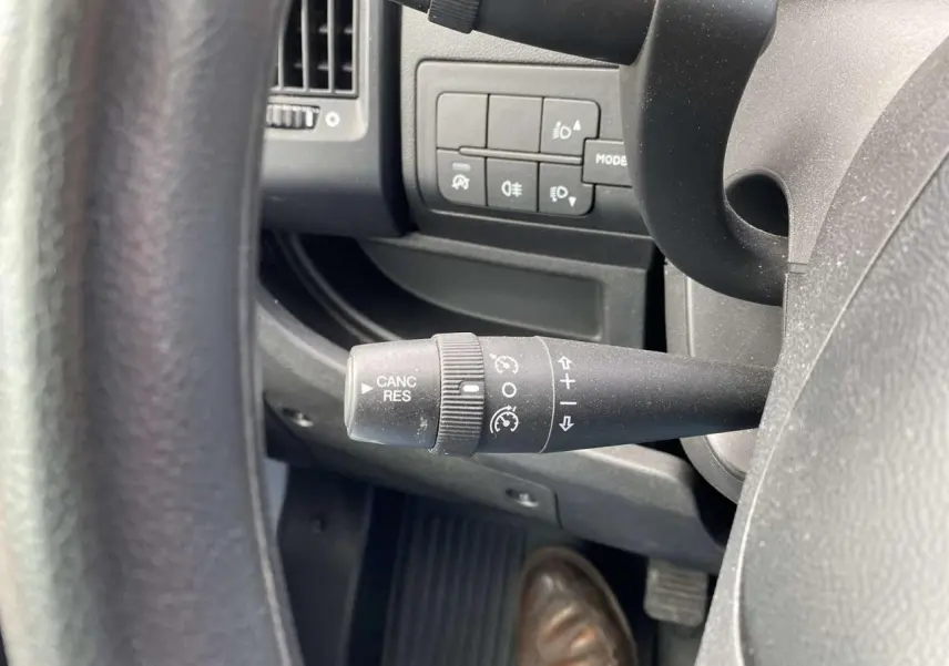 Gros plan sur la commande de régulateur de vitesse noire à gauche du volant dans l'habitacle d'un Opel Movano blanc.