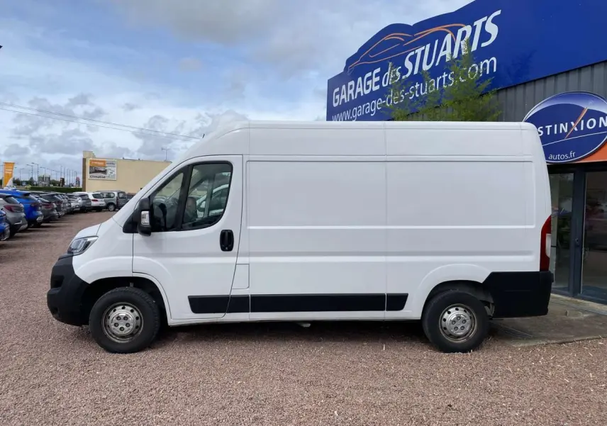 Profil latéral droit d'un fourgon blanc Opel Movano 3.5T L2H2 2022 garé devant un garage, sans marquages visibles.