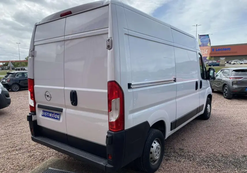 Vue 3/4 arrière droite d'un Opel Movano Fourgon blanc avec portes battantes tôlées et pare-chocs noir.
