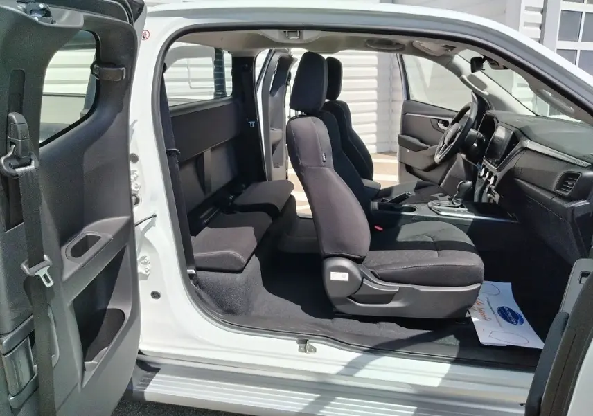 Vue latérale intérieure du pick-up Isuzu D-MAX blanc 2026, montrant les sièges avant et arrière en tissu noir.
