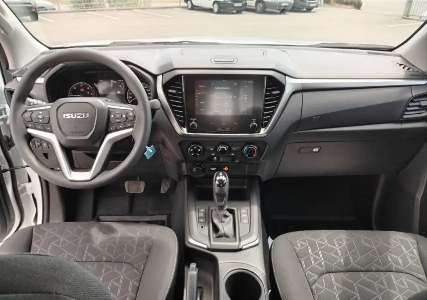 Vue intérieure avant de l'Isuzu D-MAX 2026 avec tableau de bord noir et volant multifonction.