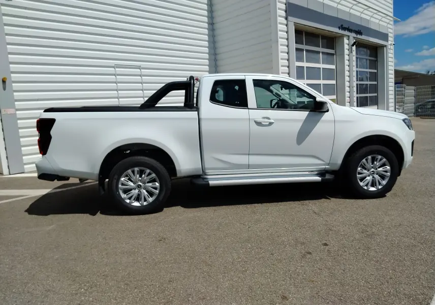 Isuzu D-MAX blanc en 3/4 avant droit, avec arceau et volet couvre benne roulant visible sur un parking extérieur.
