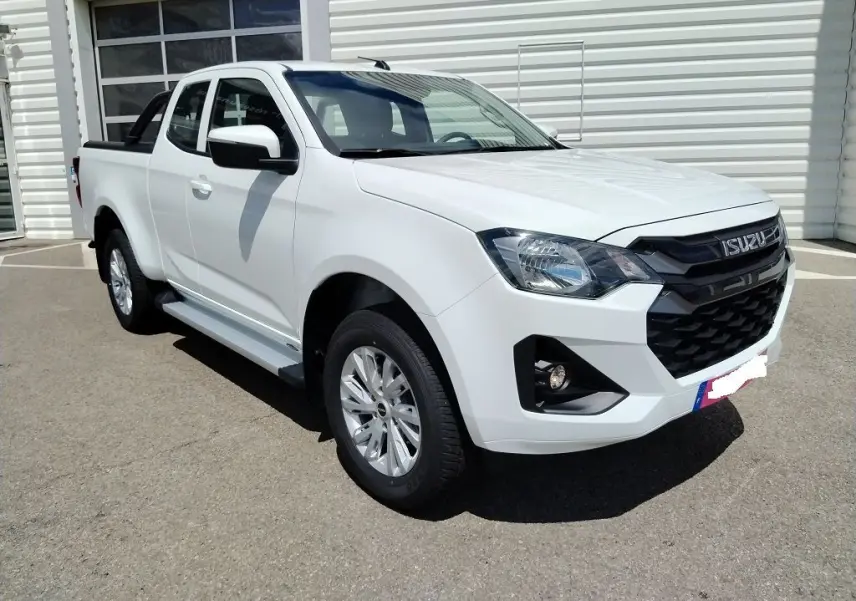 Vue 3/4 avant d'un Isuzu D-MAX blanc avec arceau et couvre benne roulant, stationné devant un bâtiment Distinxion.