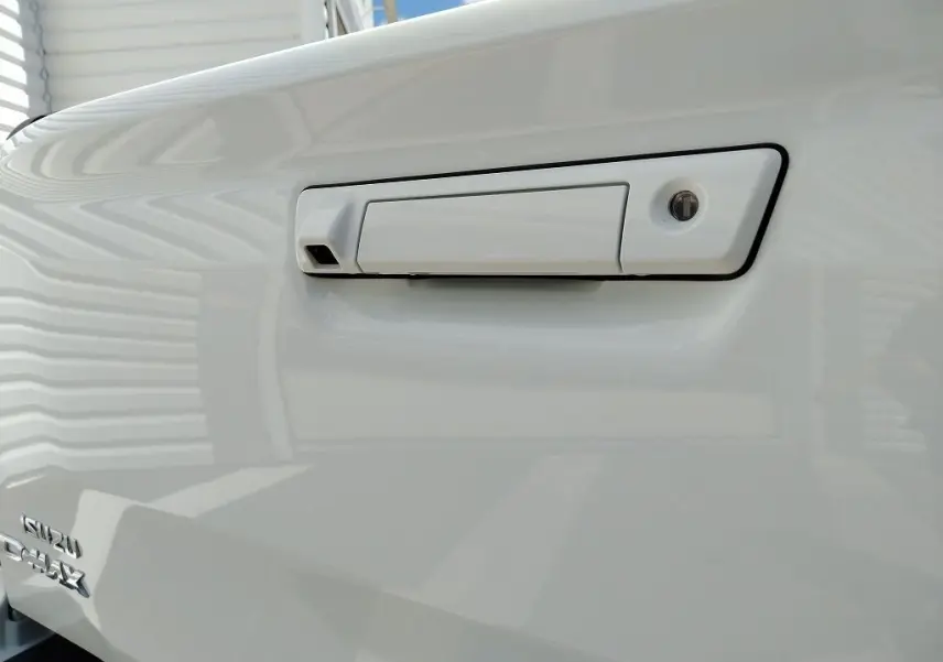 Gros plan sur la poignée blanche de la benne du pick-up Isuzu D-MAX 2026 avec logo visible en bas à gauche.