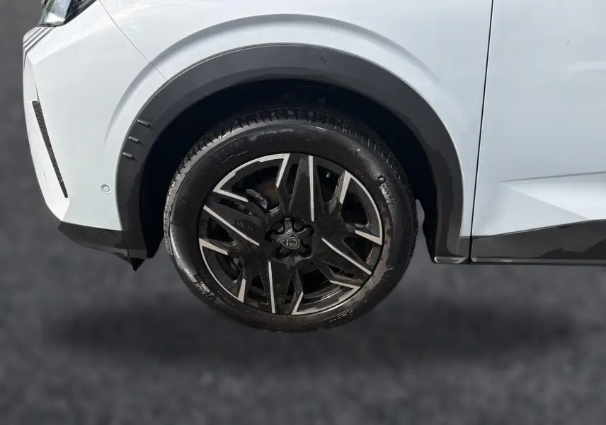Gros plan sur la roue avant droite d’un Peugeot 5008 blanc avec jante alliage noire et argentée.